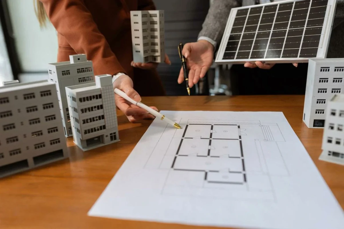 Inwestorzy i projektanci omawiają model budynku i panele fotowoltaiczne, planując ekologiczną inwestycję dla wspólnoty mieszkaniowej.