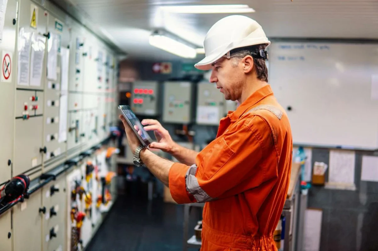 Inżynier monitorujący system fotowoltaiczny i kompensację mocy biernej za pomocą tabletu w sali sterowania elektroenergetycznego.