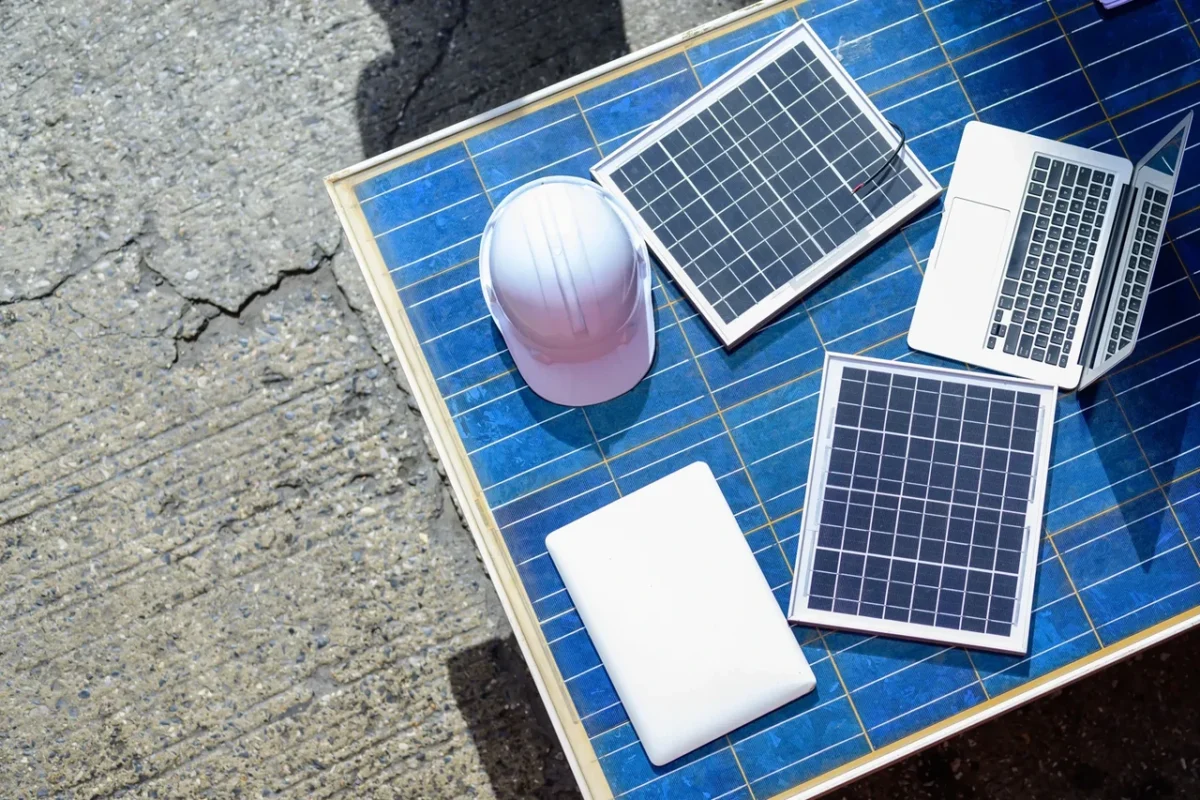 Panele słoneczne, kask ochronny i urządzenia elektroniczne umieszczone na dużym panelu fotowoltaicznym, wykorzystywane do projektowania systemów fotowoltaicznych na miejscu oraz przeprowadzania kontroli technicznych