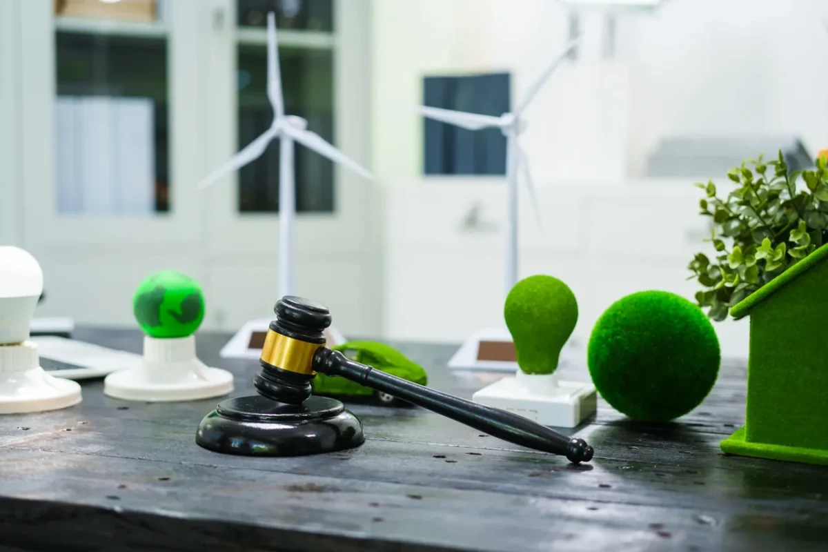 Młotek i dekoracje nawiązujące do zielonej energii (turbiny wiatrowe, ekologiczne żarówki) na stole symbolizują ramy prawne i regulacyjne regulujące energię odnawialną i działanie VPP.