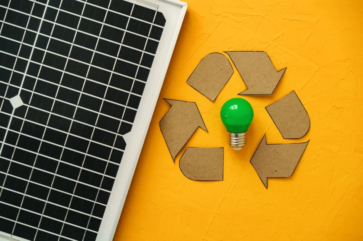 Panel fotowoltaiczny z symbolem recyklingu i zieloną żarówką, ilustrujący gospodarkę obiegu zamkniętego i recykling systemów PV