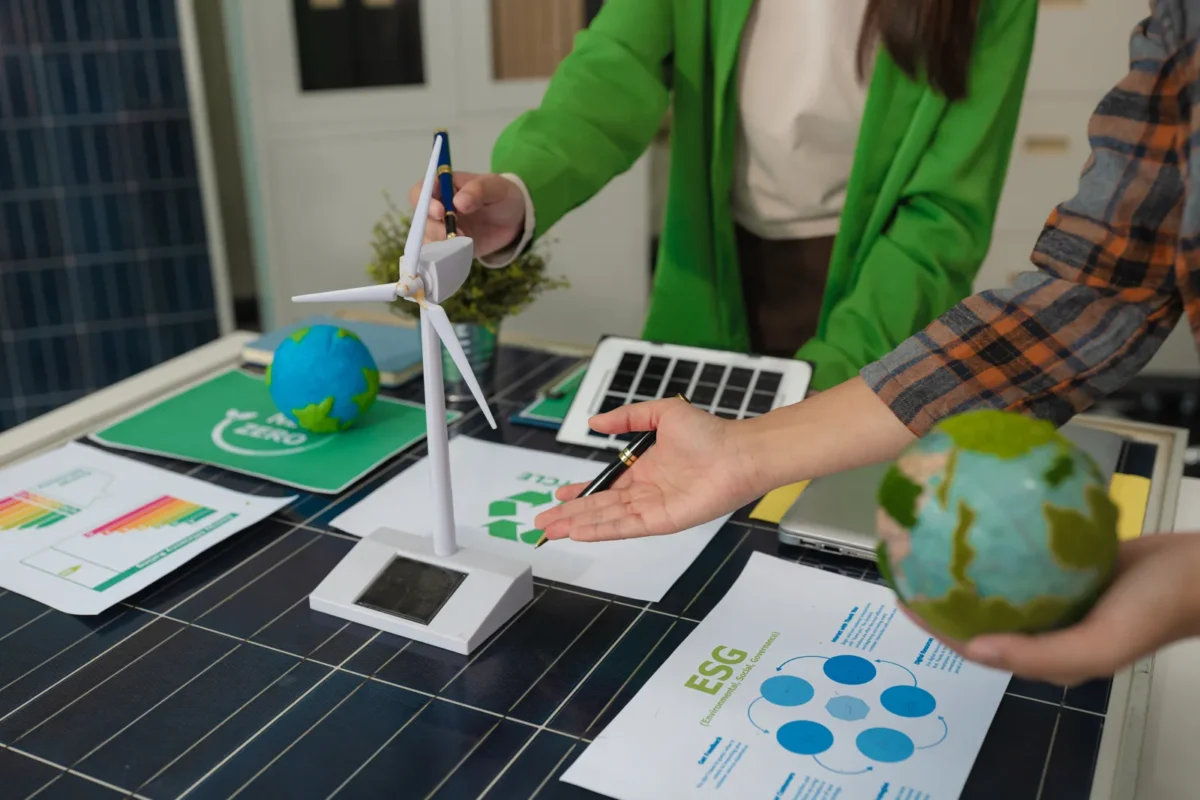 Spotkanie biznesowe z modelem turbiny wiatrowej, rekwizytami w postaci paneli słonecznych i dokumentami ESG na stole z panelami słonecznymi, omawiane są zrównoważone rozwiązania energetyczne dla hoteli.