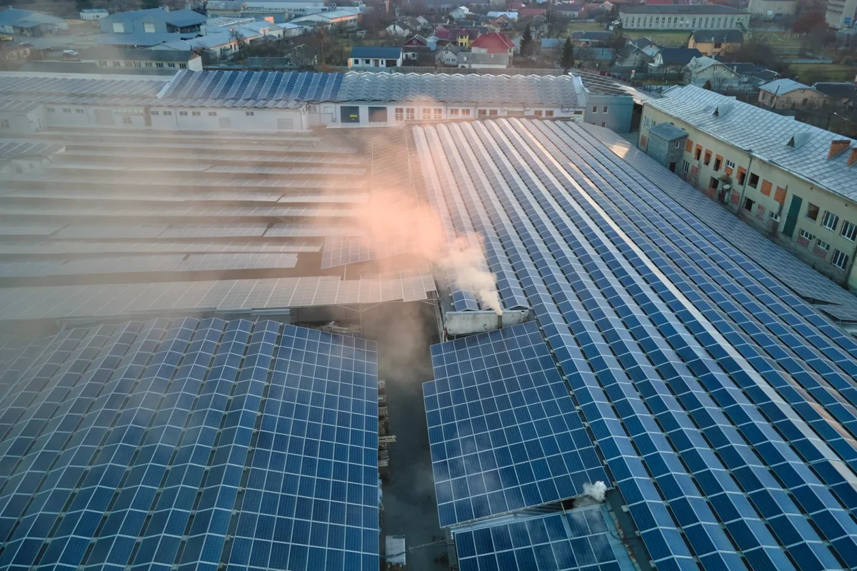 Widok z lotu ptaka na panele słoneczne zamontowane na dachach budynków przemysłowych, służące do wytwarzania odnawialnej energii elektrycznej w zapylonym środowisku przemysłowym.