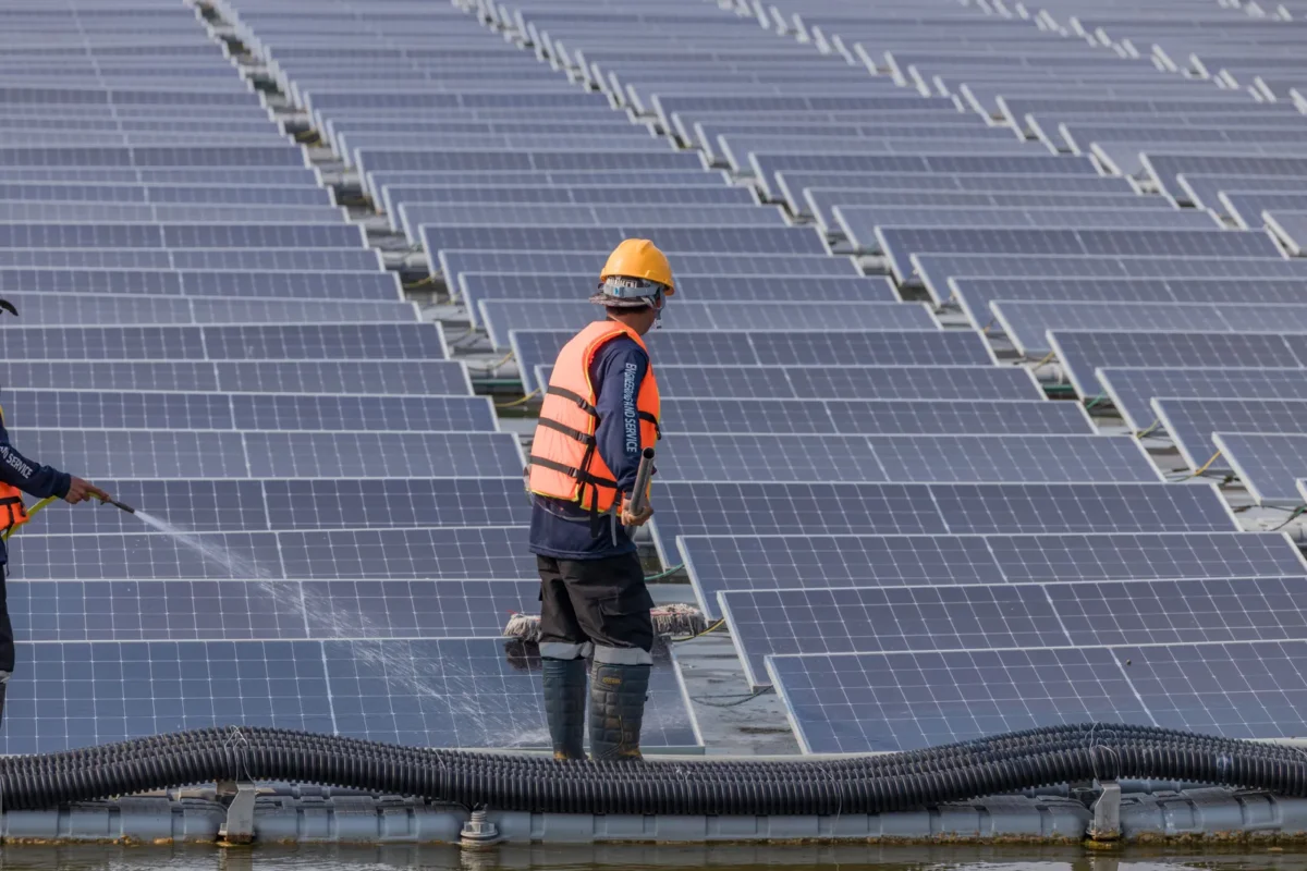 Pracownicy czyszczą pływające panele słoneczne wodą, usuwając kurz i brud, aby przywrócić wydajność wytwarzania energii w farmie słonecznej na skalę przemysłową.
