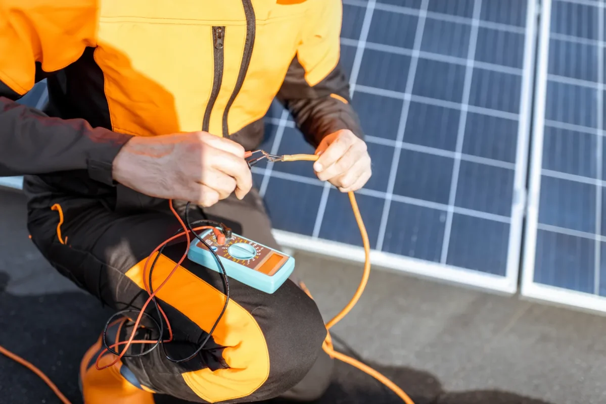 Technik wykonujący pomiary elektryczne przy panelach fotowoltaicznych za pomocą multimetru