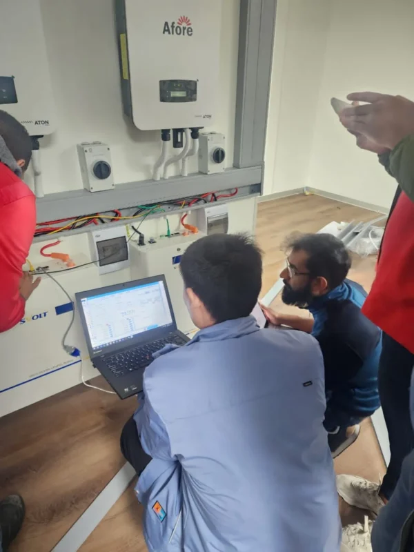 Serwisanci konfigurują nowy falownik fotowoltaiczny za pomocą laptopa podczas wymiany.