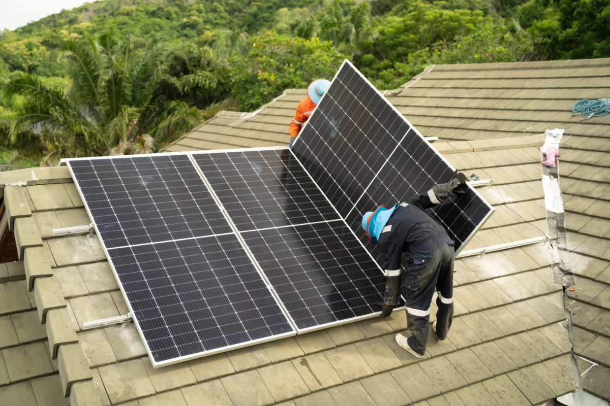 Dwóch fachowców montuje zestaw paneli słonecznych na dachu budynku, realizując montaż domowej instalacji hybrydowej z magazynem energii.