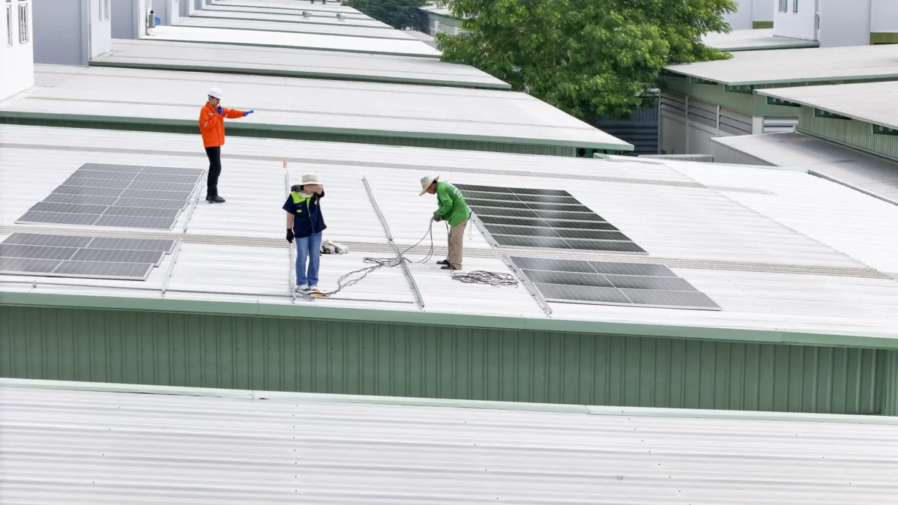 Zespół fachowców montuje moduły fotowoltaiczne na dachu hal przemysłowych podczas realizacji instalacji solarnej dla potrzeb przedsiębiorstwa.