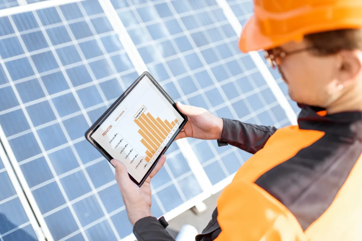 Technik w stroju roboczym analizuje dane produkcji energii na tablecie bezpośrednio przy zainstalowanych panelach instalacji fotowoltaicznej dla przedsiębiorstwa.