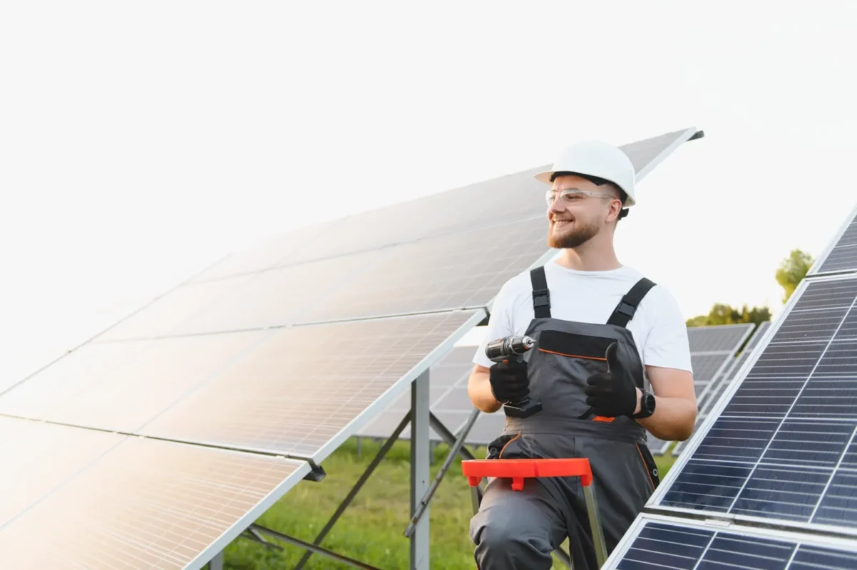 Specjalista montujący panele słoneczne trzyma wiertarkę i podnosi kciuk, przygotowując instalację do zasilania magazynu energii o pojemności 50 kWh.