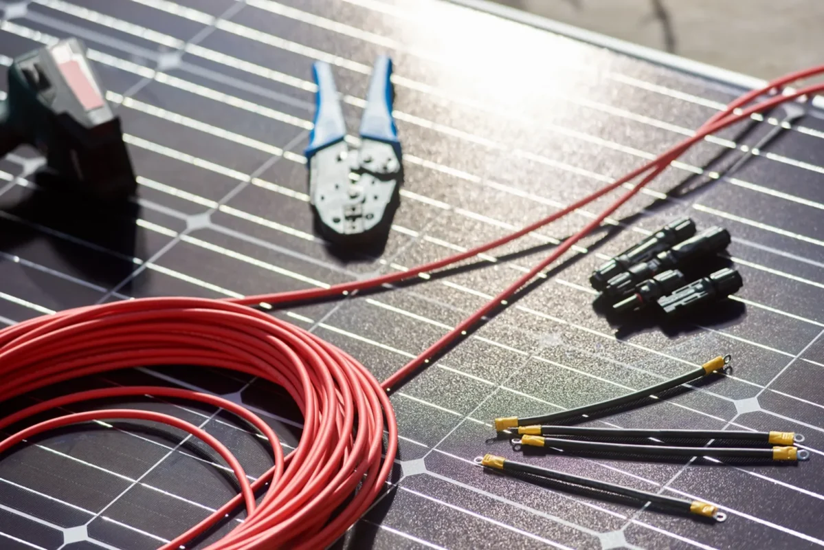 Narzędzia do okablowania słonecznego, przewody miedziane i złącza MC4 leżą na panelu fotowoltaicznym podczas montażu instalacji z magazynem energii 50 kWh.