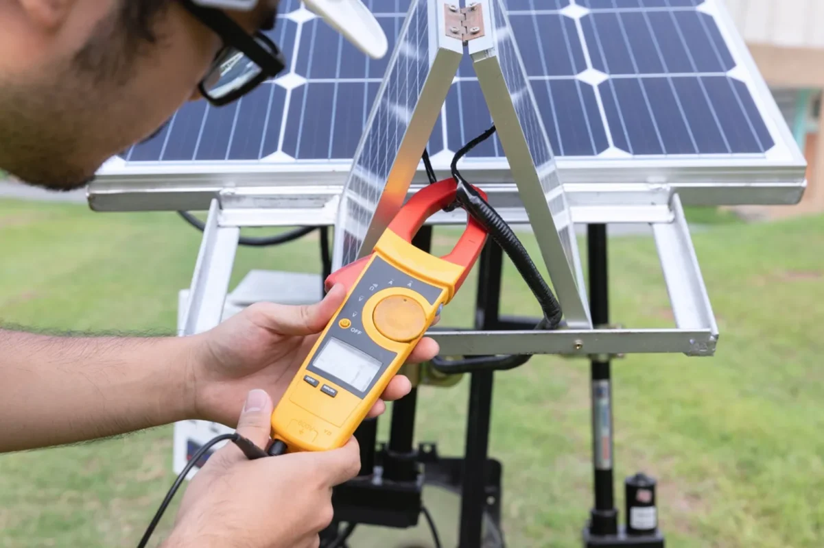 Technik mierzy prąd wyjściowy z paneli słonecznych za pomocą miernika szczękowego przed podłączeniem do magazynu energii 50 kWh.