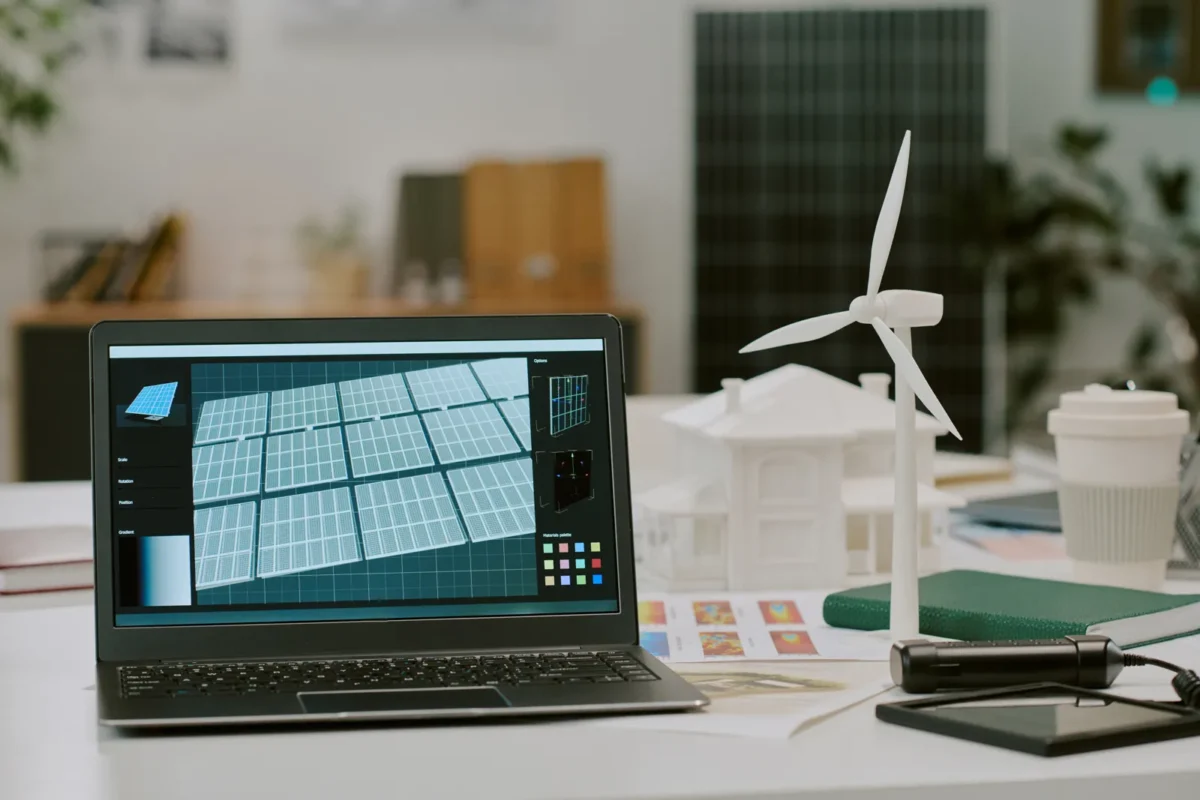 Inżynier projektuje na laptopie konfigurację instalacji magazynu energii AC coupled, obok znajdują się makieta budynku oraz model turbiny wiatrowej.