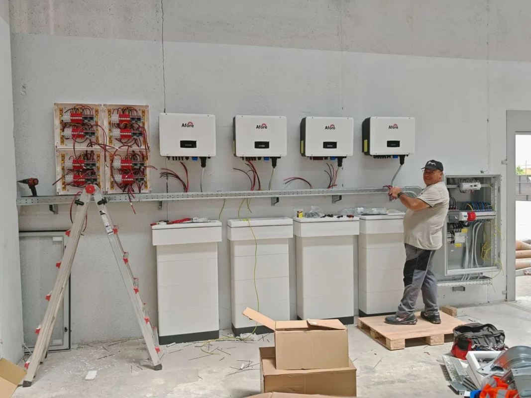 Monter wykonuje podłączenie przewodów do falowników i magazynów energii, kompletując domową instalację fotowoltaiczną pracującą w sieci z siecią zewnętrzną.