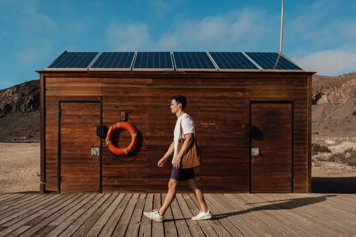 Mężczyzna spaceruje przed drewnianym budynkiem z zainstalowanymi panelami off-grid.
