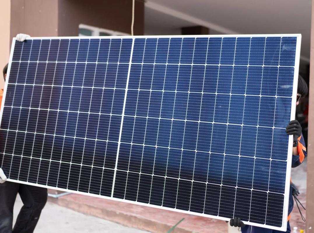 Dwie osoby w rękach trzymają duży moduł fotowoltaiczny przygotowany do montażu w domowym zestawie zasilania off-grid.