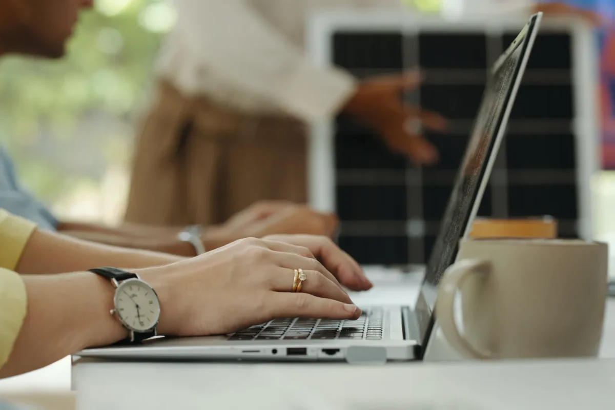 Pracownicy biurowi korzystają z laptopów podczas pracy, zużywając nadwyżkę energii wytworzoną przez pobliską instalację paneli fotowoltaicznych.
